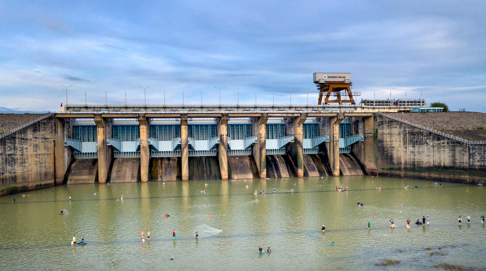 A scenic view of a dam with people fishing below under an overcast sky.